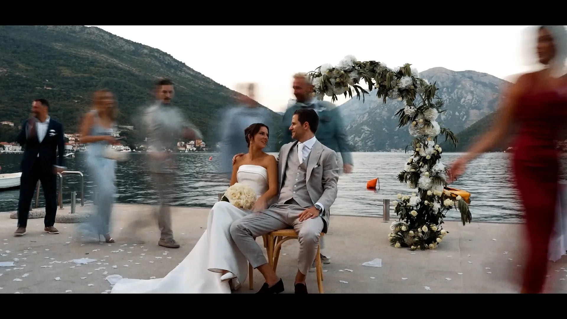 A couple seated by the water while guests pass, Montenegro